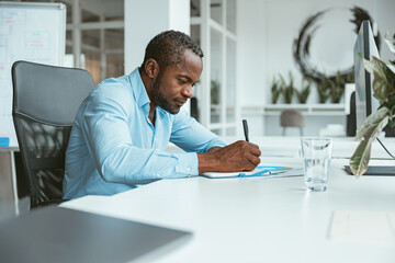 Confident African businessman taking notes while sitting in modern office
