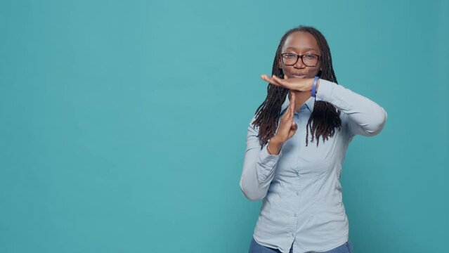 Female model doing timeout pause gesture on camera, showing t shape stop symbol with arms in studio. Refusing and rejecting problem to do pause sign and feel serious, signal no.