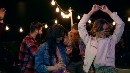 On the rooftop of terrace group of friends have fun time dancing and feeling happy at the party night time they drinking champagne