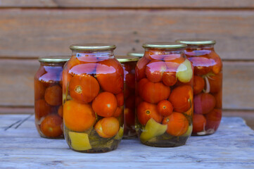 Some glass jars with canned tomatoes with iron lids stand on a wooden table. home storage solution, saving leftovers, canning concept, rustic composition