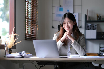 Obraz premium Beautiful young asian woman sitting at coffee shop using laptop. Happy young businesswoman sitting at table in cafe with tab top computer.