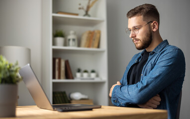 Obraz premium Young handsome man working on laptop at home, thoughtful male coding on computer remotely