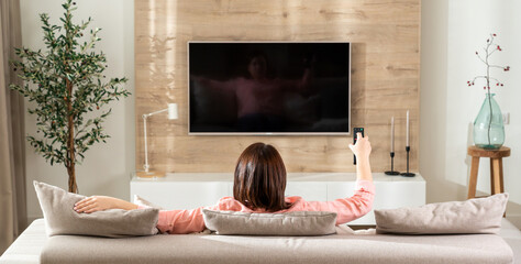 The girl on the sofa changes channels on the TV in a modern living room
