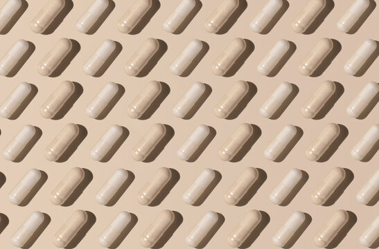 Creative pattern with capsules on light beige top view, hard shadows. Taking supplements