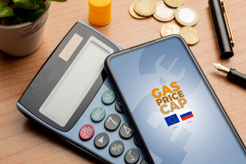 Gas price cap concept: smartphone over a calculator on a wooden table sorrounded by some euro coins
