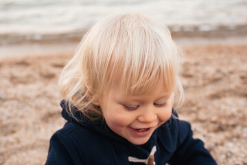 portrait of smiling baby boy sitting on sand on beach in autumn time