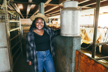 Obraz na płótnie Canvas Young african farmer woman holding milk churn inside cowshed - Focus on face