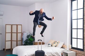 Young hispanic man business worker jumping on bed at hotel room