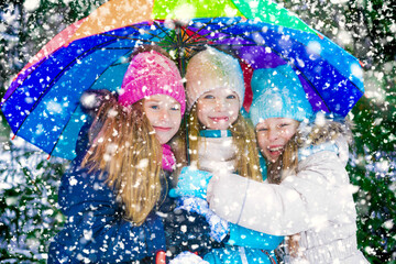Three blond little girls smiling in snowfall under umbrella.