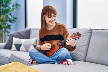 Young woman playing ukelele sitting on sofa at home