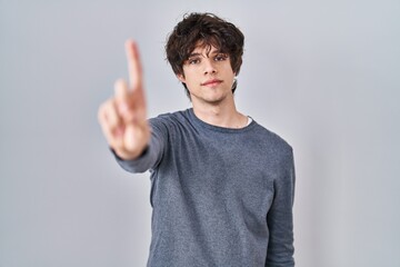 Young man standing over isolated background pointing with finger up and angry expression, showing no gesture