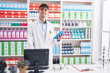 Young hispanic man pharmacist using computer and touchpad at pharmacy