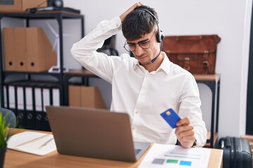 Young hispanic man working using computer laptop holding credit card confuse and wondering about...