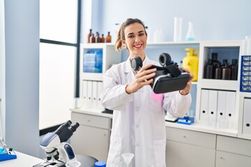 Young woman wearing scientist uniform holding virtual reality goggles at laboratory