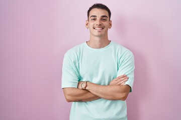 Handsome hispanic man standing over pink background happy face smiling with crossed arms looking at the camera. positive person.