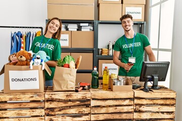 Young hispanic volunteer couple smiling happy working at charity center.