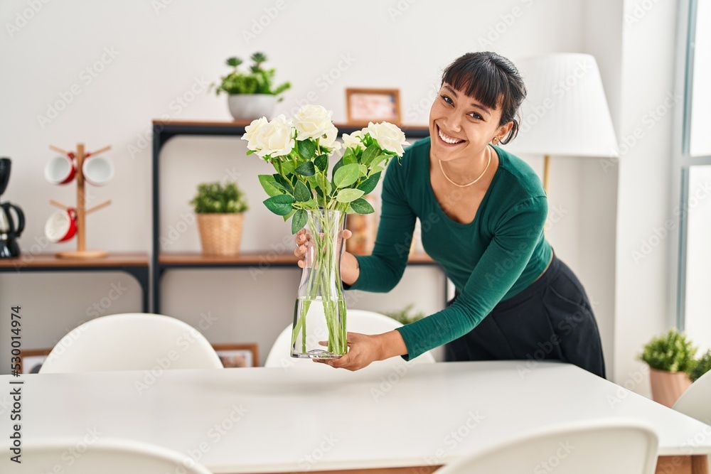 Sticker young beautiful hispanic woman smiling confident putting plant pot on table at home