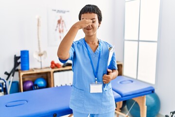 Obraz premium Young hispanic woman with short hair working at pain recovery clinic smelling something stinky and disgusting, intolerable smell, holding breath with fingers on nose. bad smell