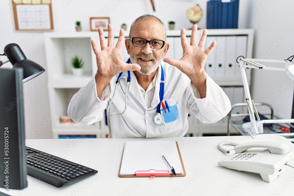 Poster Mature doctor man at the clinic showing and pointing up with fingers number ten while smiling confident and happy.