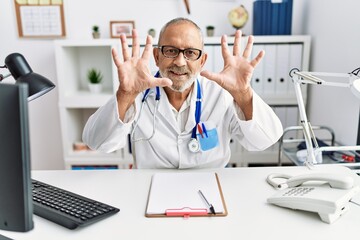 Mature doctor man at the clinic showing and pointing up with fingers number ten while smiling confident and happy.