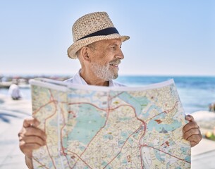 Senior man smiling confident wearing summer hat holding map at seaside
