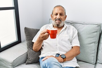 Senior grey-haired man smiling confident drinking coffee at home