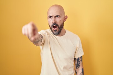 Hispanic man with tattoos standing over yellow background pointing with finger surprised ahead,...