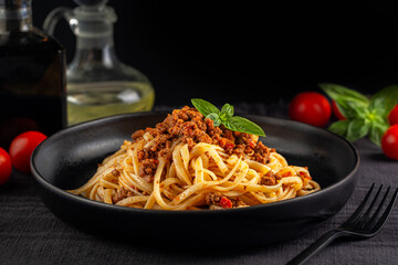 Italian dinner with Spaghetti or linguine with meat and tomato sauce bolognese on a black plate and dark background. Copy space. - obrazy, fototapety, plakaty