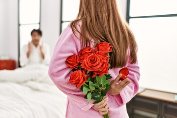 Woman surprising her boyfriend with bouquet of roses at bedroom.