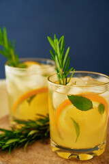 Homemade lemonade with orange and rosemary, Glass of summer coctail on dark background, Citrus detox water for refreshing in hot summer day