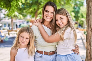 Obraz premium Mother and daughters smiling confident hugging each other standing at park