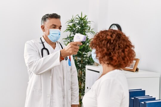 Middle age man and woman wearing doctor uniform and medical mask measuring temperature at clinic