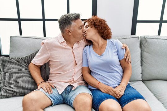 Middle age man and woman couple hugging each other and kissing sitting on sofa at home