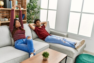 Fototapeta premium Young latin couple tired yawning and stretching arms sitting on the sofa at home.