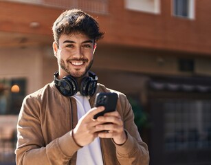 Young hispanic man smiling confident using smartphone at street