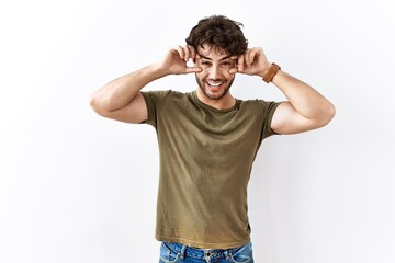 Fototapeta premium Hispanic man standing over isolated white background trying to open eyes with fingers, sleepy and tired for morning fatigue