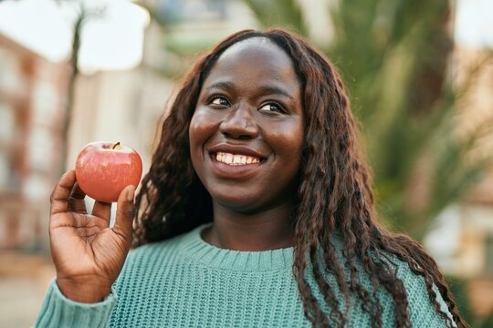 Young african woman smiling happy holding fresh red apple at the city