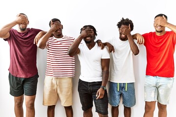 Young african group of friends standing together over isolated background smiling and laughing with hand on face covering eyes for surprise. blind concept.