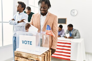 Young american voter man smiling happy putting vote in voting box at electoral center.