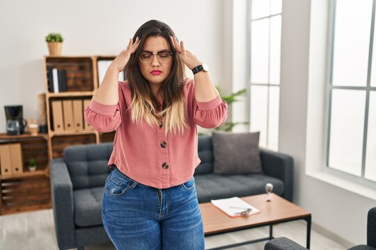 Young hispanic woman working at the office wearing glasses with hand on head, headache because stress. suffering migraine.