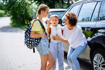 Smiling happy mother bringing daughter and son back to school saying goodbye on car parking. outdoor. Single mom, school, family, education outdoor concept.