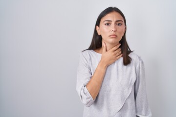 Young hispanic woman standing over white background touching painful neck, sore throat for flu, clod and infection