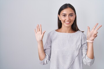 Young hispanic woman standing over white background showing and pointing up with fingers number eight while smiling confident and happy.