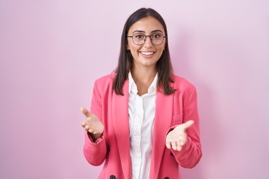 Young hispanic woman wearing business clothes and glasses smiling cheerful offering hands giving assistance and acceptance.
