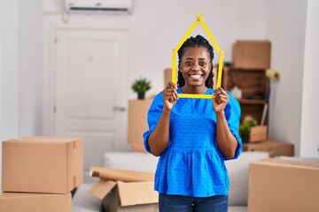 African woman with braided hair at new home holding ruler smiling with a happy and cool smile on...