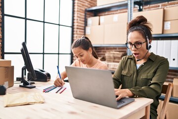 Young mother and daughter working at the office and doing homework scared and amazed with open mouth for surprise, disbelief face