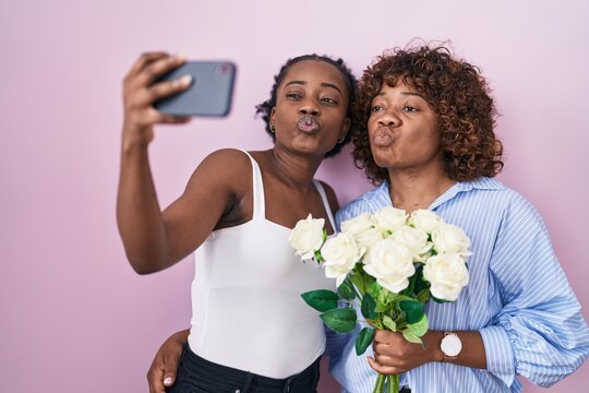 Two african women taking a selfie photo with flowers looking at the camera blowing a kiss being lovely and sexy. love expression.