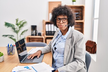 Black woman with curly hair wearing call center agent headset at the office skeptic and nervous, frowning upset because of problem. negative person.