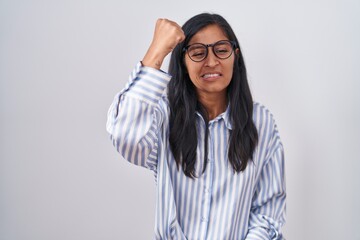 Young hispanic woman wearing glasses angry and mad raising fist frustrated and furious while shouting with anger. rage and aggressive concept.