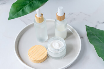 Cosmetics packaging with green herbal leaves. Set of cosmetic bottles of cream or lotion on marble background. Blank packaging. Natural beauty spa product concept. Mock-up.